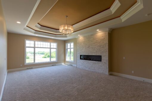 Stone Creek primary bedroom with tray ceiling and linear fireplace