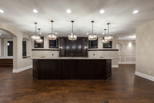 Kingfogl custom home lower-level bar with long dark island and glass pendants