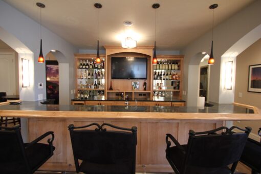 Kingfogl custom home lower-level bar with stone counter, pendants and lit back bar