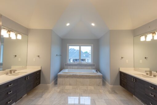 Kingfogl custom home primary bath with soaking tub between two dark vanities