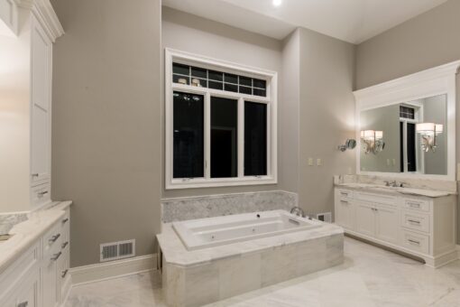 Kingfogl custom home primary bath with soaking tub beneath a window and white vanities