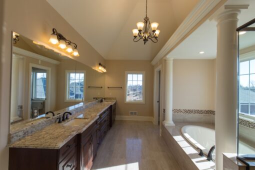 Kingfogl custom home primary bath with long dark vanity, chandelier and corner tub