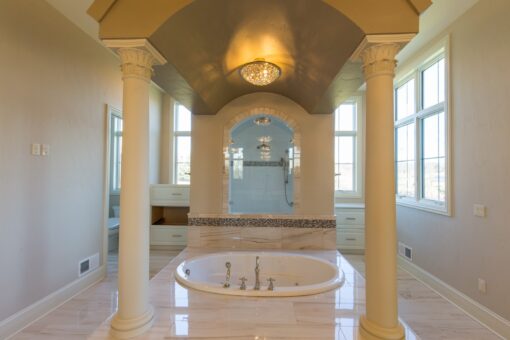 Callista primary bath tub framed by columns beneath a chandelier