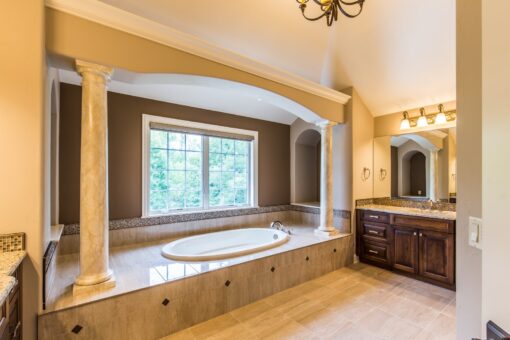 Kingfogl custom home primary bath soaking tub framed by columns beneath a window