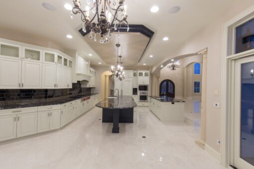 Kingfogl custom home white kitchen with dark island, crystal chandelier and marble floor