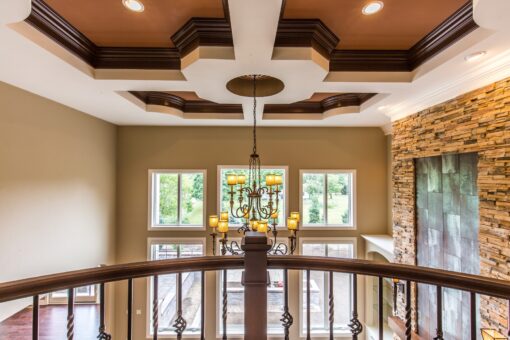 Kingfogl custom home loft overlooking a chandelier with coffered ceiling and stacked stone wall