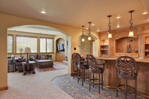 Kingfogl custom home lower-level bar with carved stools and arched opening