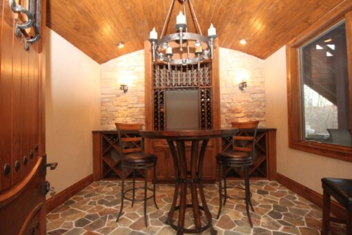 Kingfogl custom home wine tasting room with wood ceiling, stone wall and iron chandelier