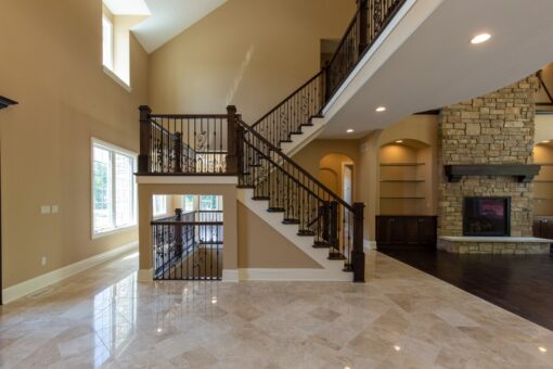 Kingfogl custom home open staircase with iron balusters beside a stone fireplace