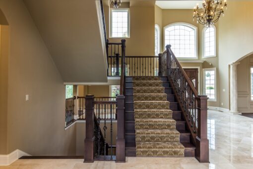 Kingfogl custom home staircase with carpet runner and iron balusters to an arched window