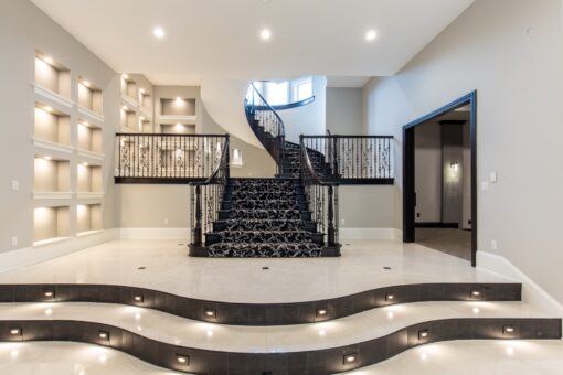 Kingfogl custom home curved staircase rising from a stepped landing with lit wall niches