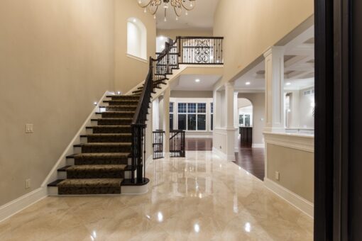 Kingfogl custom home staircase with carpet runner and iron balusters in a marble foyer