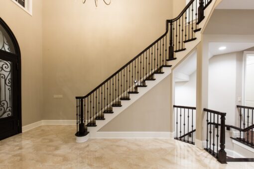 Kingfogl custom home straight staircase with iron balusters beside an arched iron door