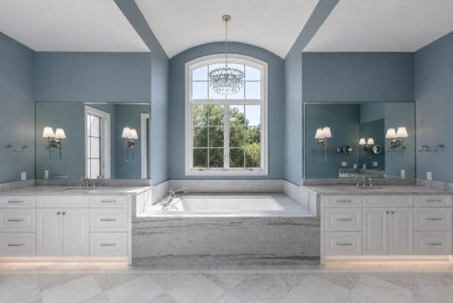 Ridge primary bath tub beneath an arched window between double vanities